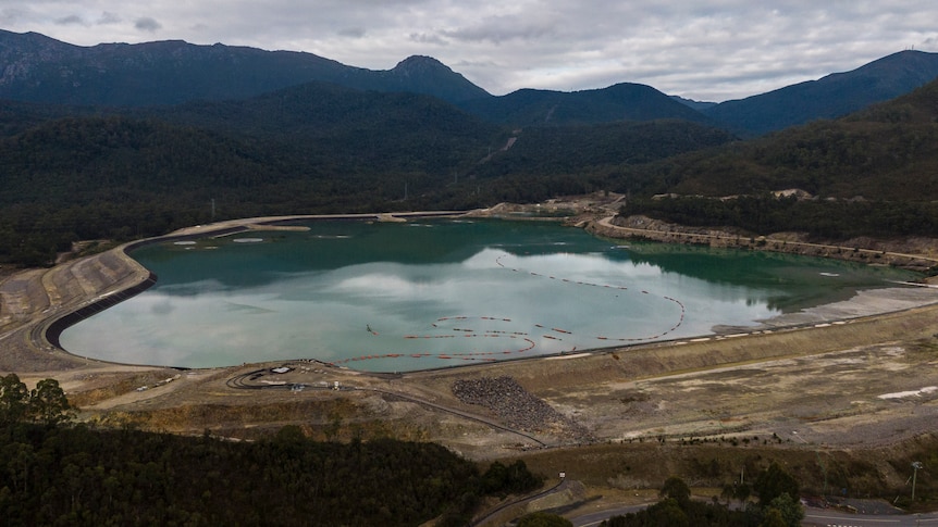 A large dam holding light-blue water surrounded by forest.