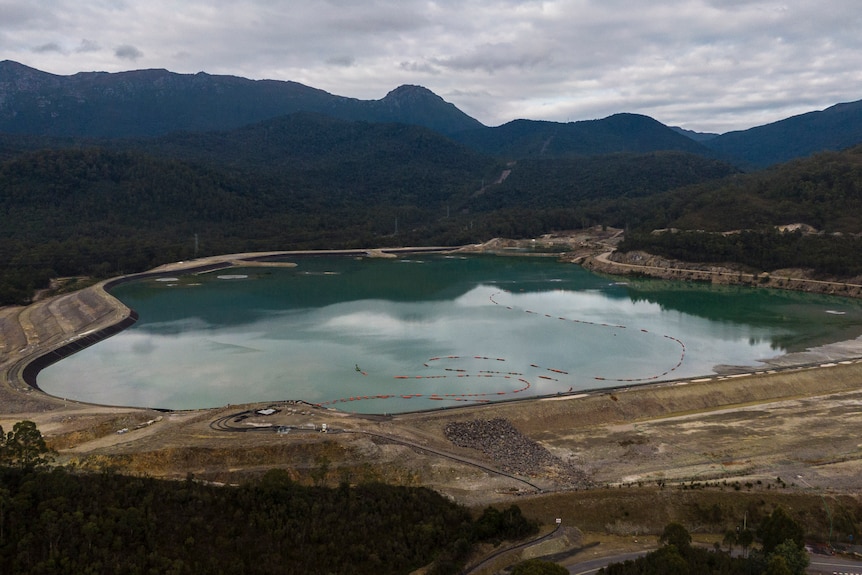 A large dam holding light-blue water surrounded by forest.