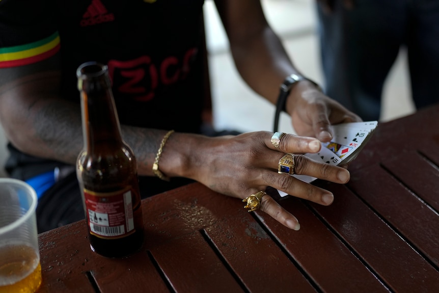 Hands holding playing cards next to a beer bottle on a table. 