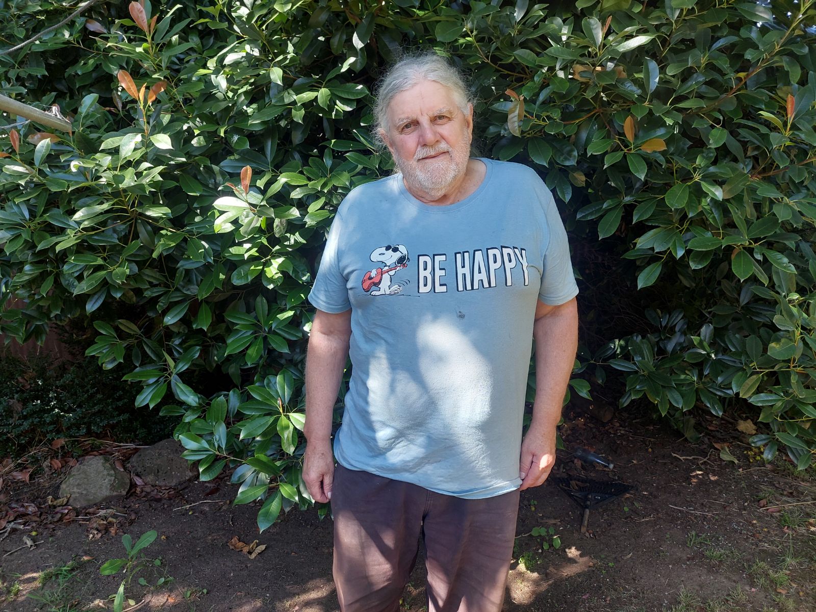 A grey-haired man in a light blue Snoopy tshirt that reads Be Happy