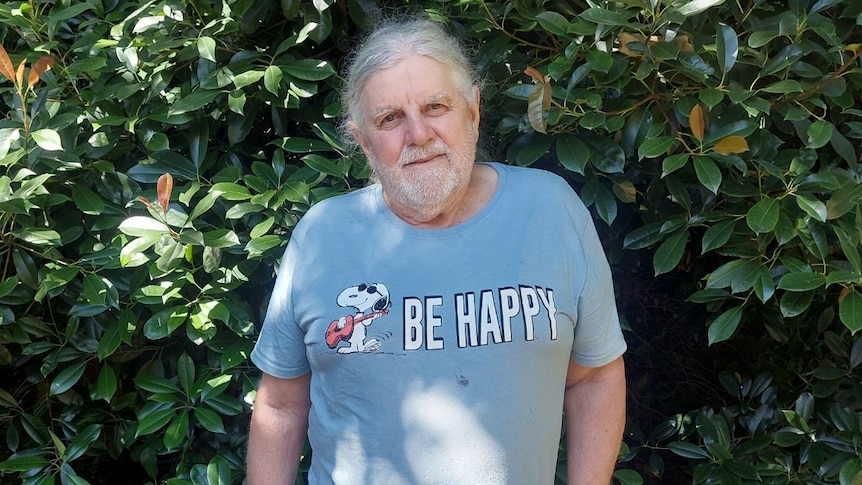 A grey-haired man in a light blue Snoopy tshirt that reads Be Happy