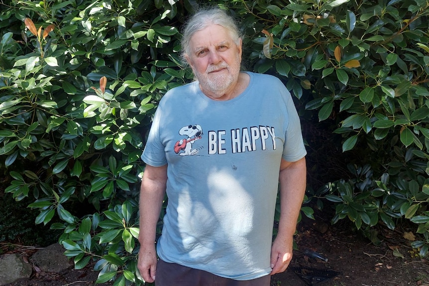 A grey-haired man in a light blue Snoopy tshirt that reads Be Happy