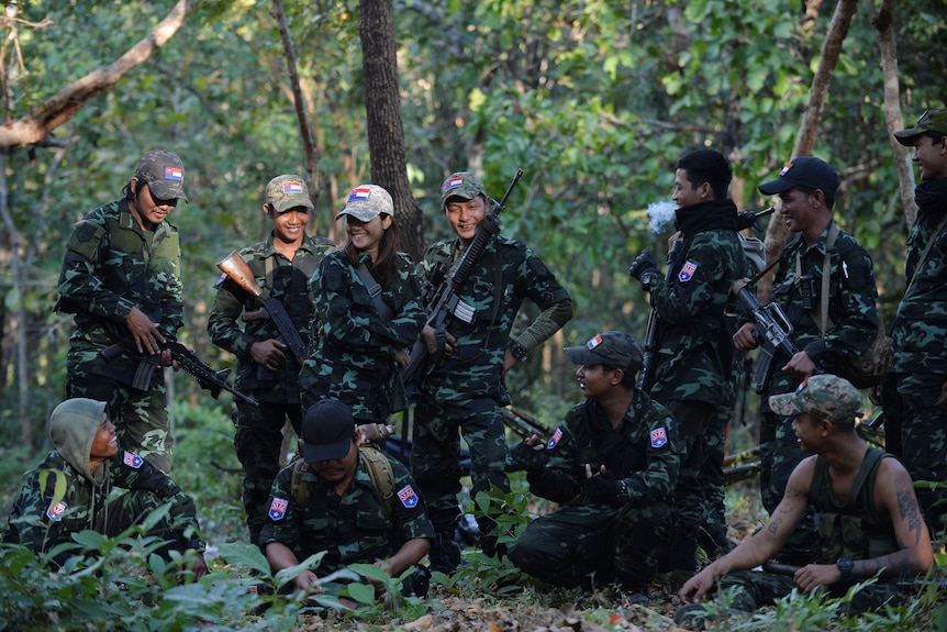 A group of young people in camo holding weapons and smiling