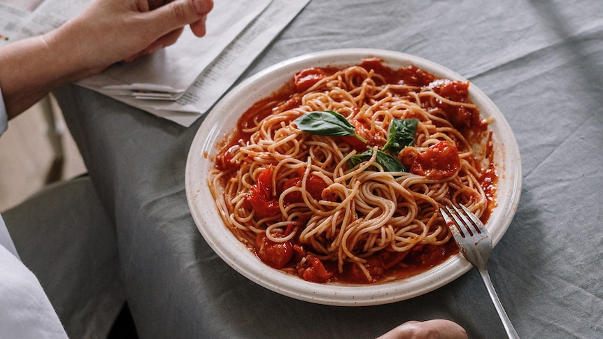 A person sits at a table before a large plate of spaghetti with tomato sauce