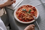 A person sits at a table before a large plate of spaghetti with tomato sauce