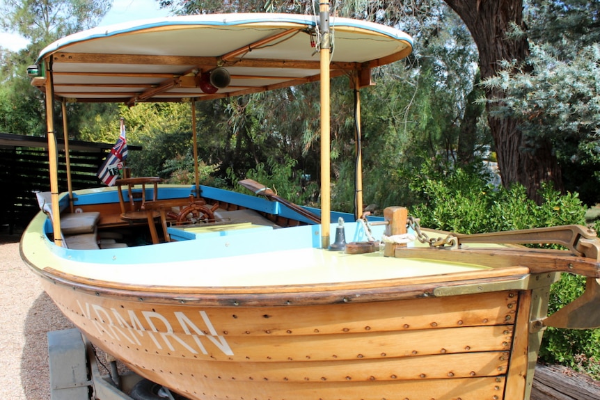 A restored wooden boat sits on the trailer in a suburban front yard.