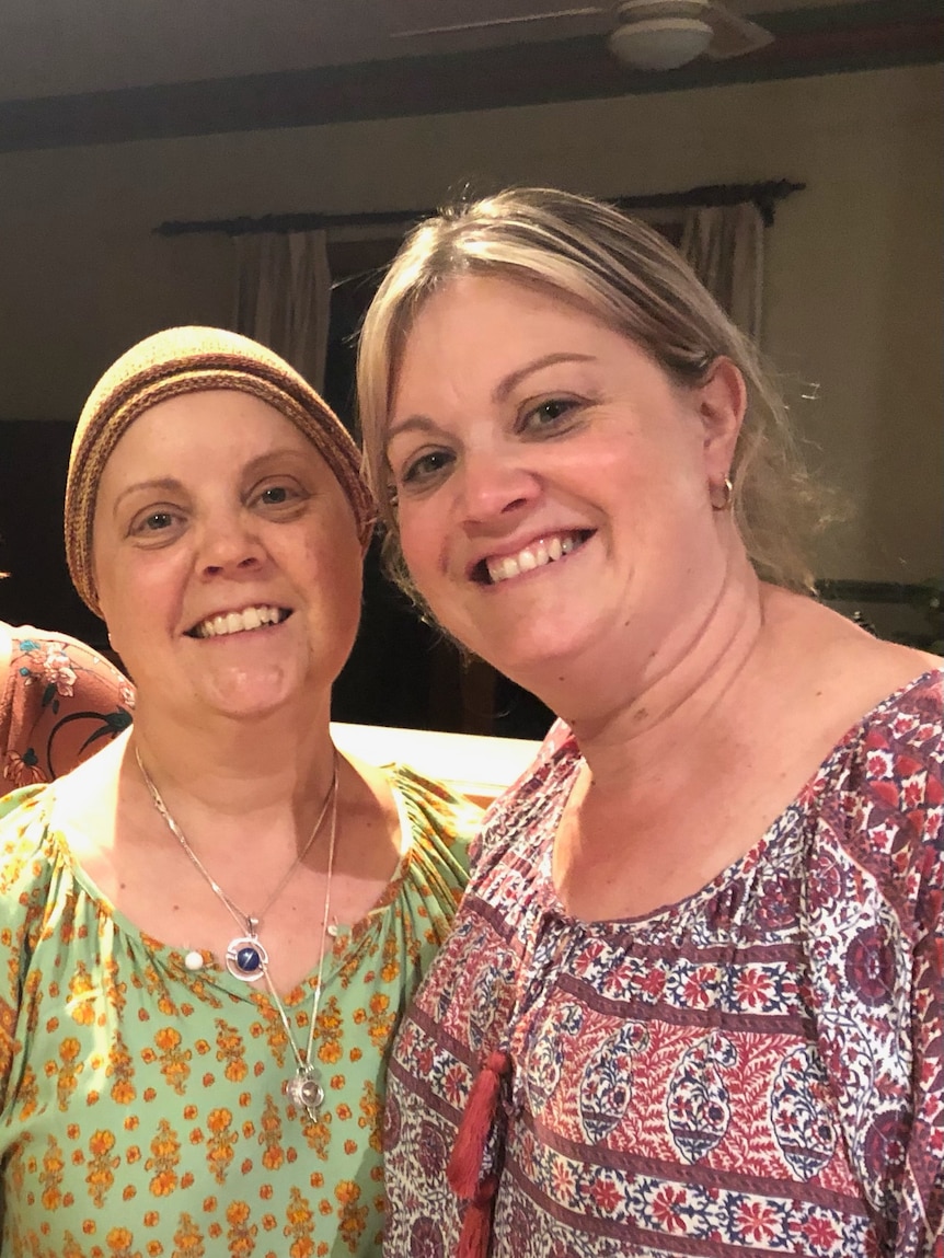 Two sisters standing together smiling, one wearing a headscarf.