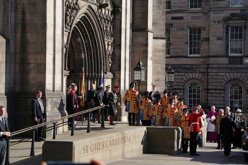 King Charles leaves a cathedral in ceremonial military dress towards a car.