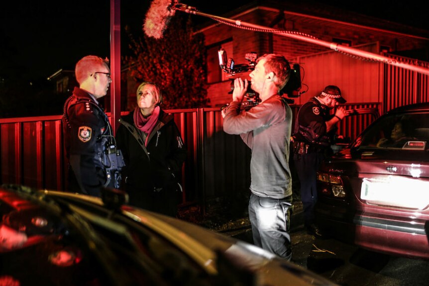 Night shot cameraman filming Ferguson interviewing policeman outside house with red eerie light from police sirens.