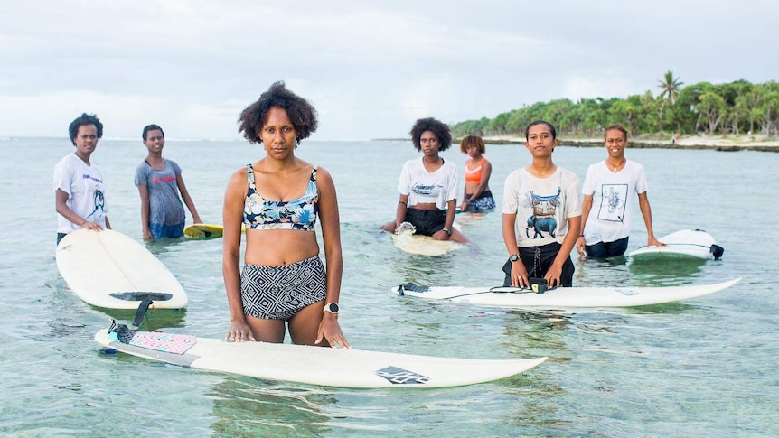 Stephanie Mahuk, with six other women, standing on the water with their surfboards.