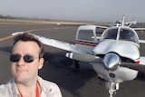 A selfie of a man in front of a small plane on a runway
