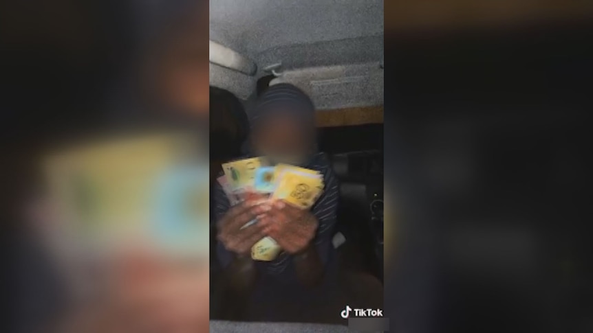 A child holding a bunch of $100 dollar notes sitting in the back of a car