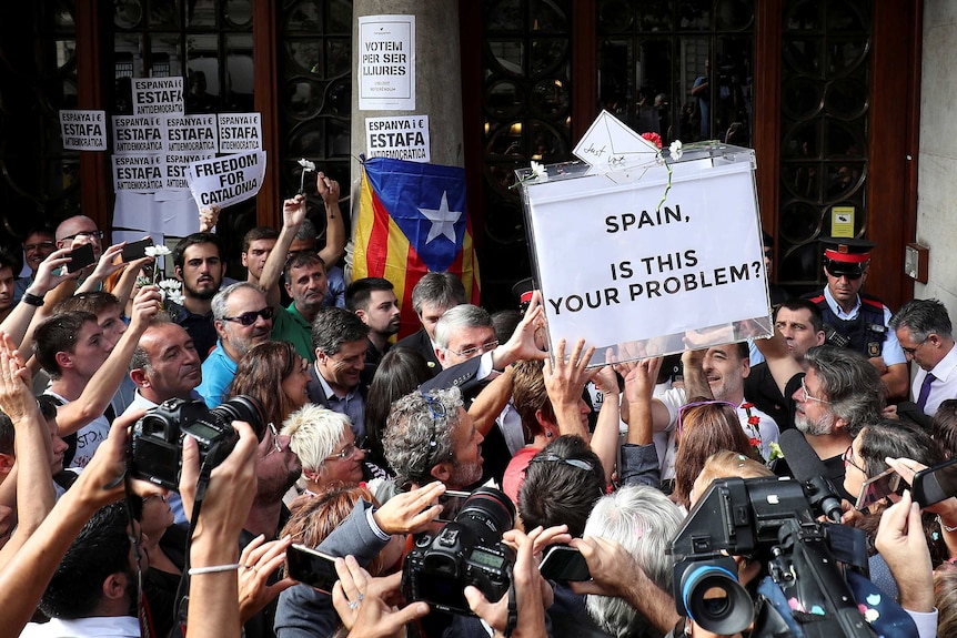 Protesters hold aloft a ballot box that reads "SPAIN, IS THIS YOUR PROBLEM?" in a crowd.
