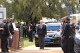 A black hearse and funeral procession arrive outside a church building.