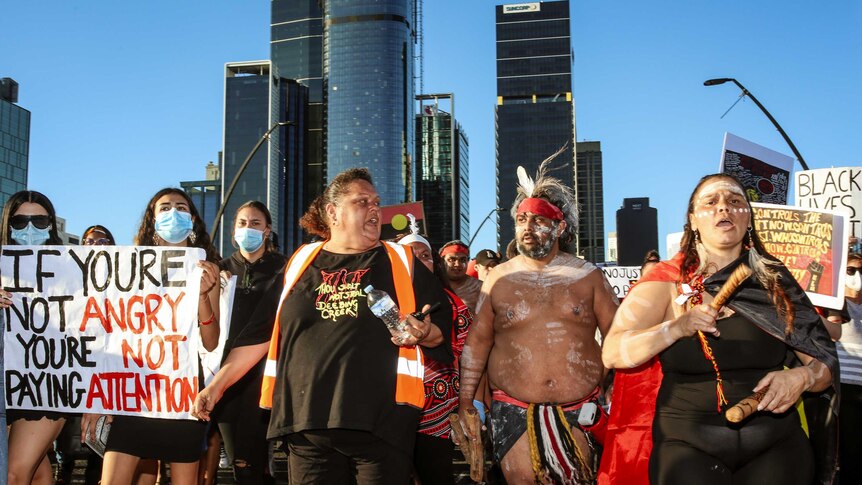 Aboriginal protesters, some wearing traditional dress, march through Brisbane.