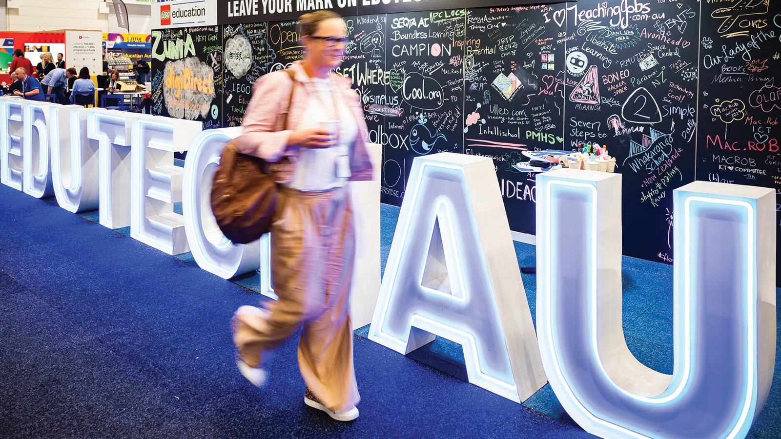 Person walking in front of an Edutech AU sign, exhibitors in the background.