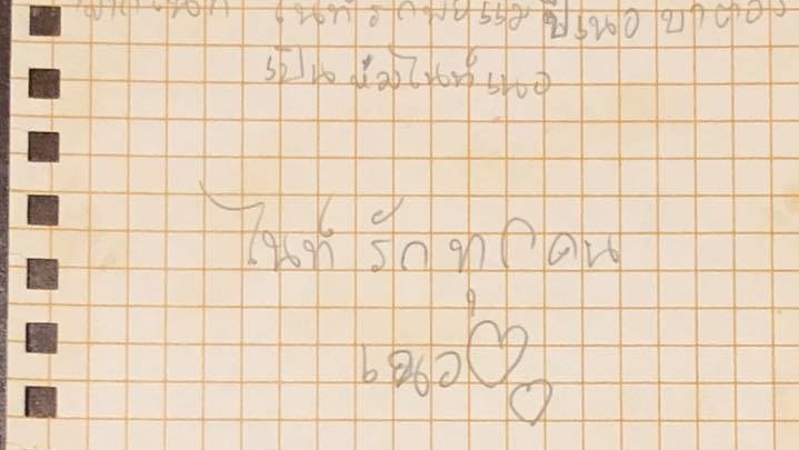 A piece of yellow paper with Thai writing in pencil.
