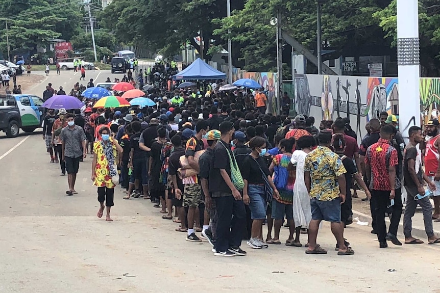 Crowds of people dressed in black with the hills of Port Moresby in the distance.