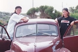 Two young women standing in the front doors of an old brown Beetle car.