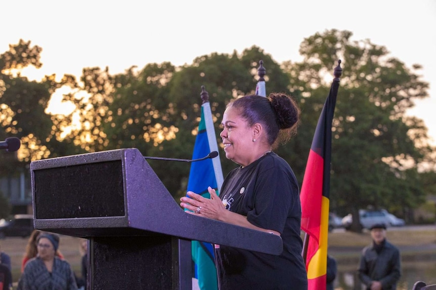 a smiling woman stands at a podium speaking