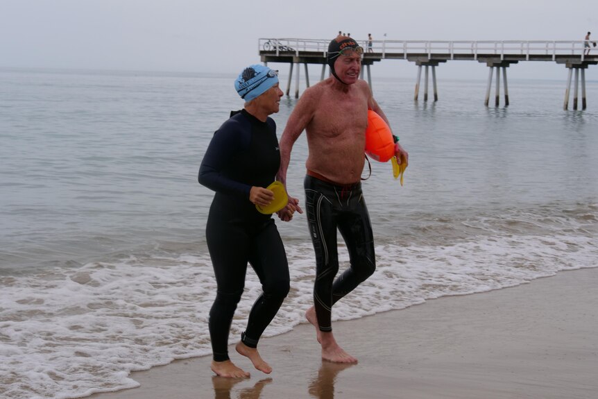Two people in wetsuits running on a beach