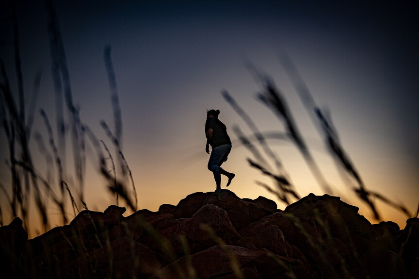 Raelene Cooper dances in silouette at sunrise on the top of red rocks in Murujuga.