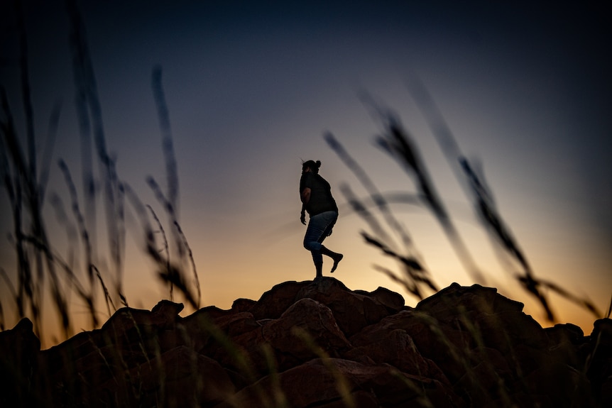 Raelene Cooper dances in silouette at sunrise on the top of red rocks in Murujuga.