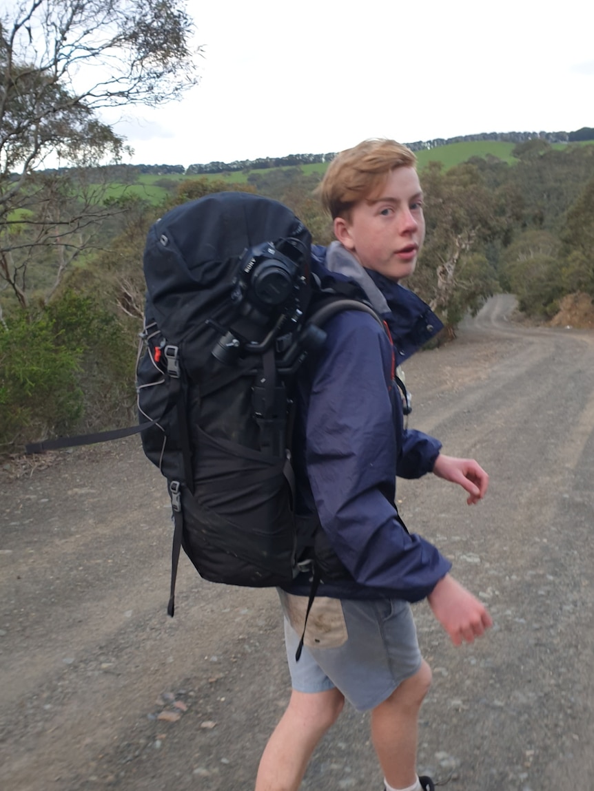 A boy with a backpack looks at the camera while walking