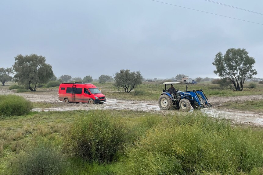 A red van being towed through boggy mud by a tractor.
