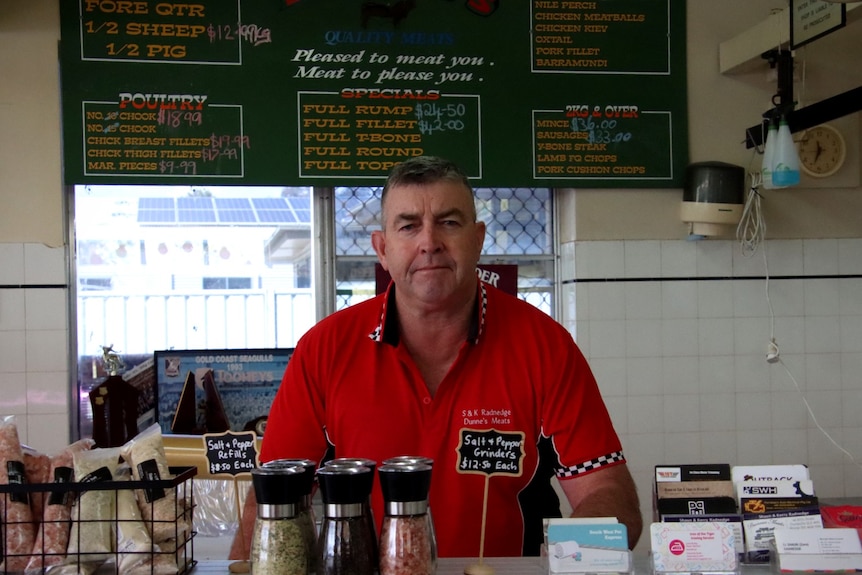 Man wearing a red shirt behind a counter looks at the camera. 