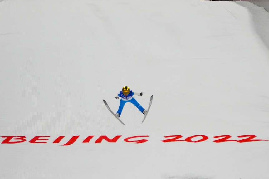 A person with a ski helmet, goggles and skis is airborne with the words Beijing 2022 behind them.