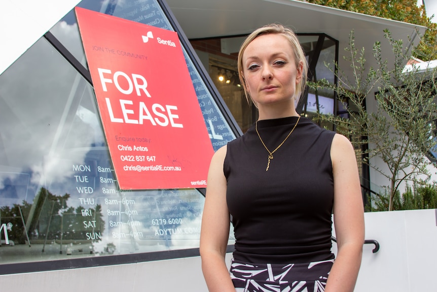 A young blonde woman in front of a business with a for lease sign.