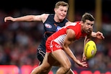 A Sydney Swans AFL player handballs in front of a GWS Giants opponent.