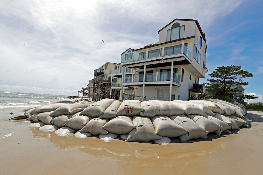 A group of houses on the beach is surrounded by piled-up sandbags