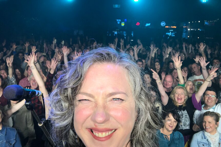 Selfie of Angie Hart on stage with a large crowd behind her