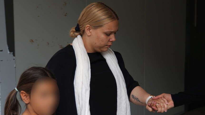 Teeana clasps a child's hand and the hand of another person out of shot as she walks out of court.