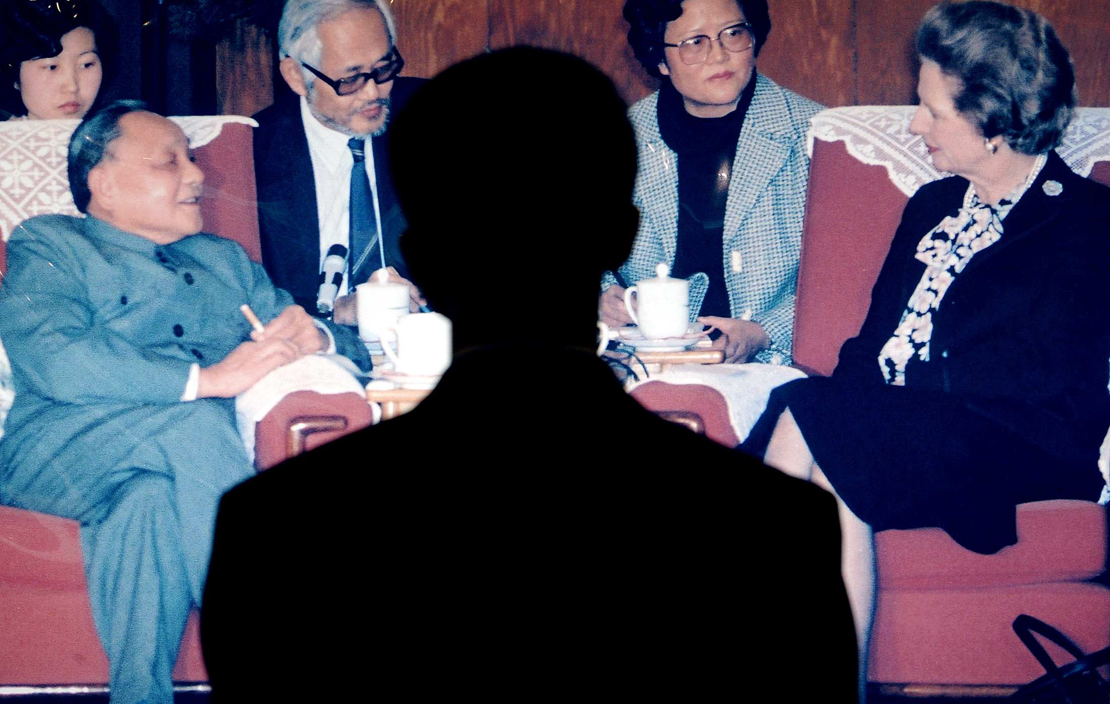 A man's shadow falls on a photo of Deng Xiaoping sitting opposite Margaret Thatcher in a meeting.