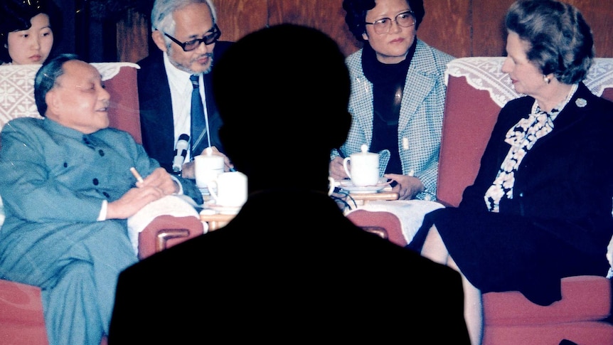 A man's shadow falls on a photo of Deng Xiaoping sitting opposite Margaret Thatcher in a meeting.