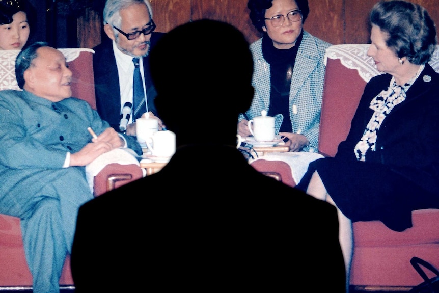 A man's shadow falls on a photo of Deng Xiaoping sitting opposite Margaret Thatcher in a meeting.