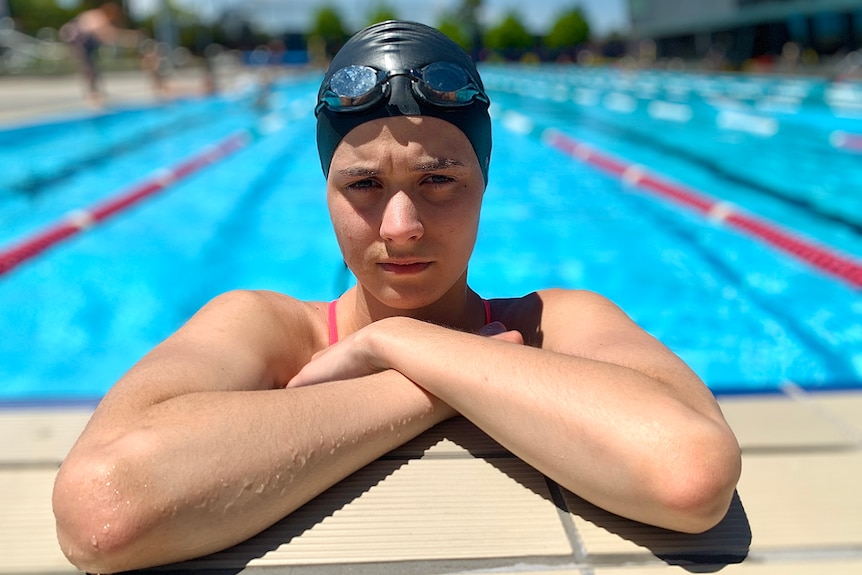 A young woman is pictured in a swimming pool, wearing a swimming cap and goggles on her head.