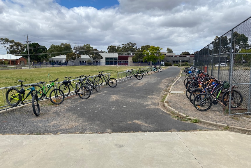 A series of bikes parked near a tennis court on a cloudy day.