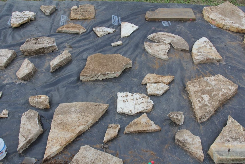 Pieces of broken headstone on black plastic sheet