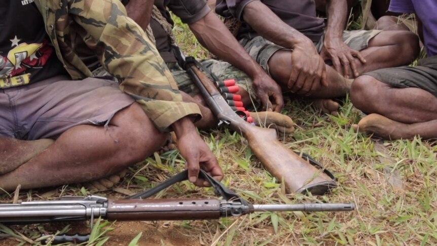 Men sit down cross-legged in PNG's highlands with their rifles and ammunition.