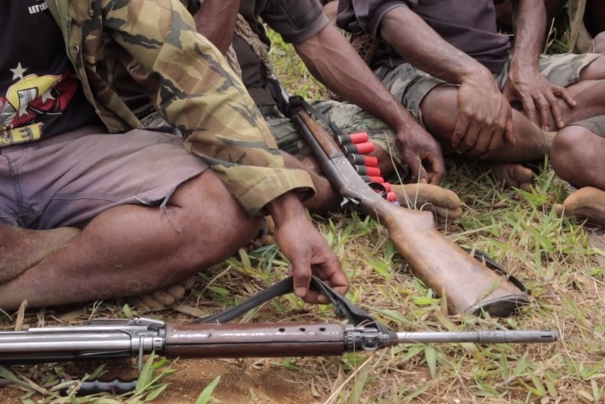 Men sit down cross-legged in PNG's highlands with their rifles and ammunition.