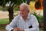 A man sits at a table looking downcast with a green background