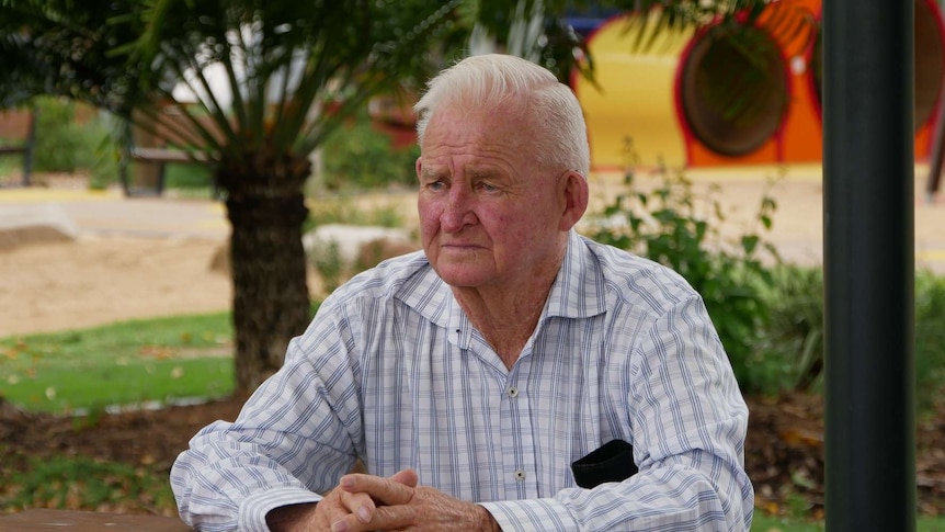 A man sits at a table looking downcast with a green background