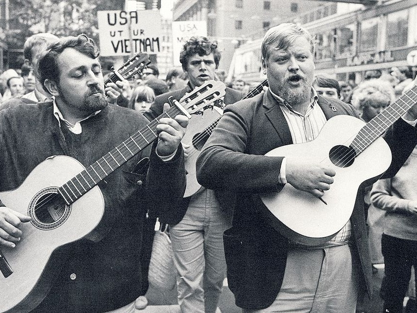 Musicians fronting a group protesters walking down street while playing guitars.