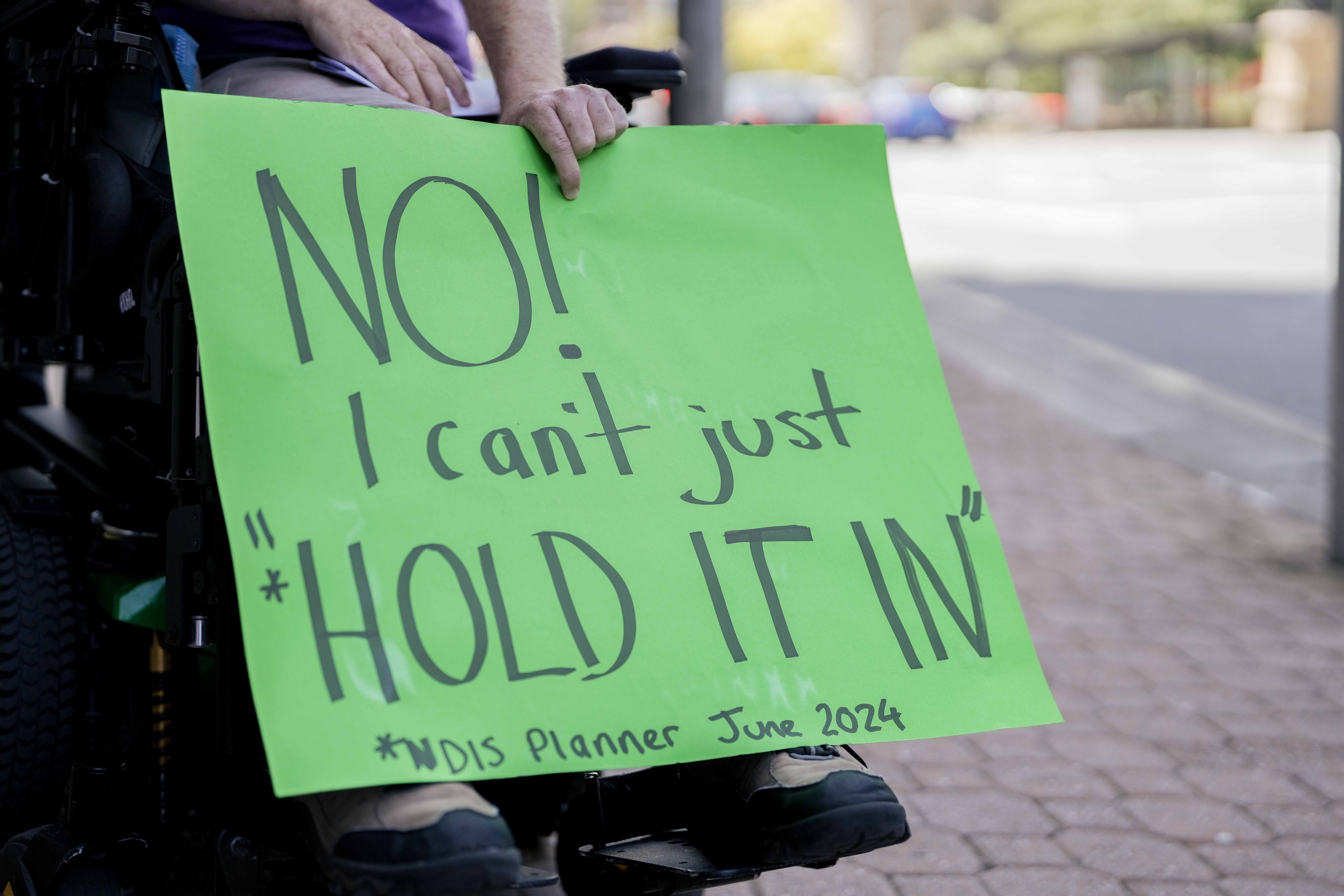 A man in a wheelchair protests with others holding signs