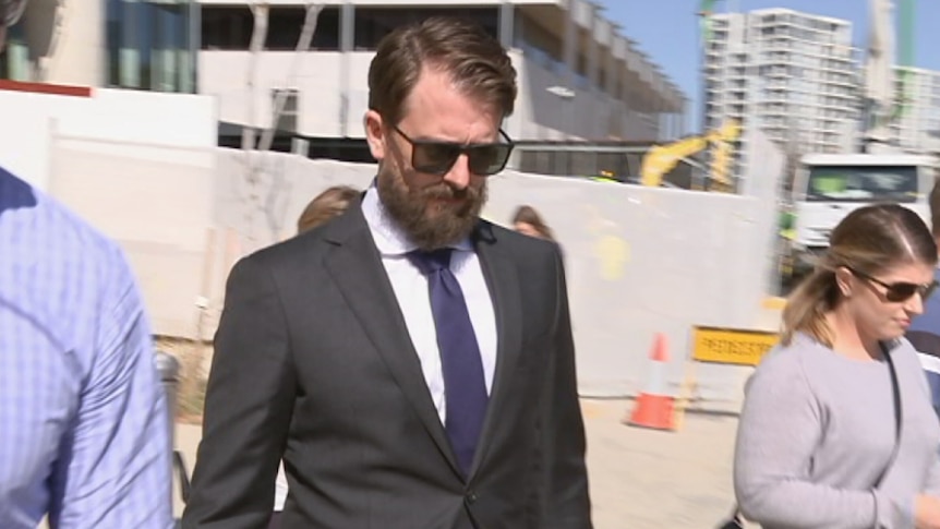 A beared man in a suit leaves the court building.