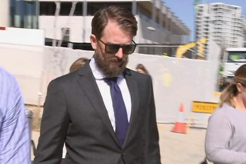 A beared man in a suit leaves the court building.